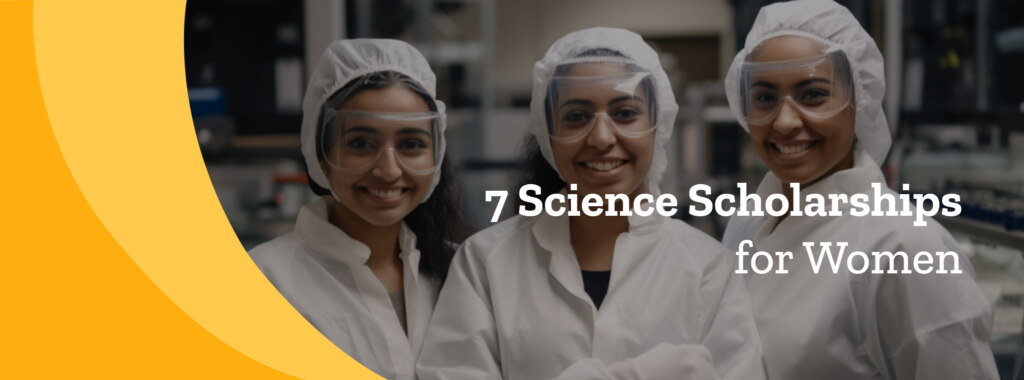 Three young female scientists in white lab coats, safety glasses and white head coverings smile at the camera